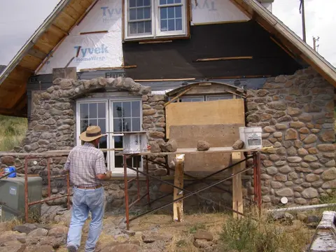 A worker is building a stone wall on the exterior of a house.