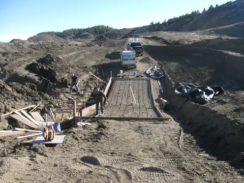 A wide shot shows construction workers on a hillside excavation site.