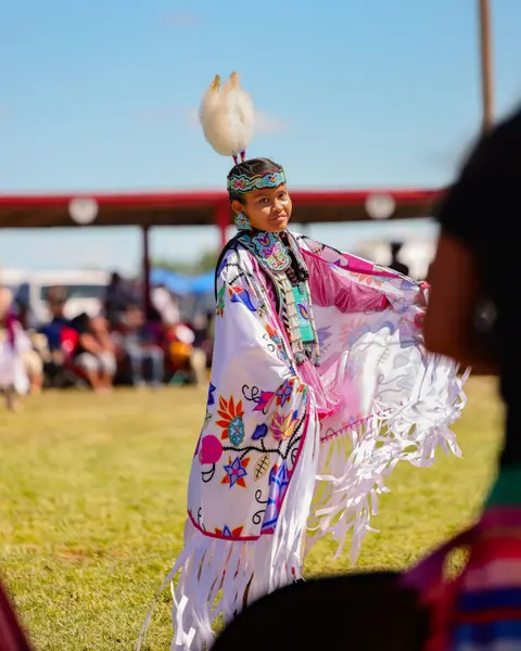 A young person in traditional regalia dancing outdoors.