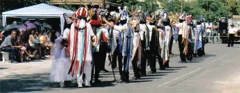 People in elaborate costumes and masks participate in an outdoor parade.