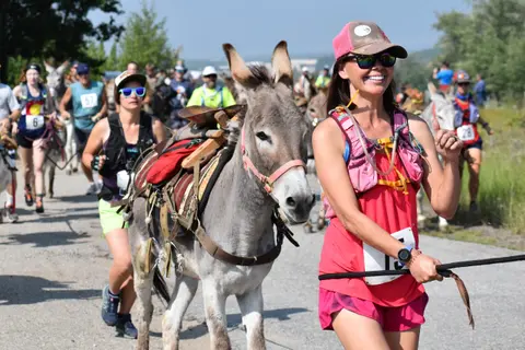 A woman smiles while running alongside a pack donkey during a race.
