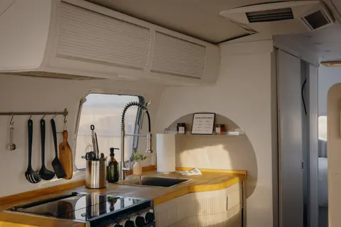 A modern minimalist RV interior featuring a compact kitchen with wooden countertops and white cabinets.