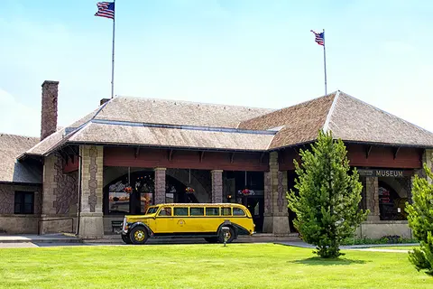A yellow vintage tour bus parked in front of a stone building with flags on poles.