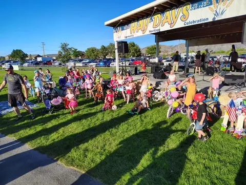 A large group of children and adults gathered on a lawn near a stage.