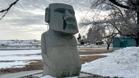 A large stone statue resembling a moai stands outdoors in a snowy landscape.