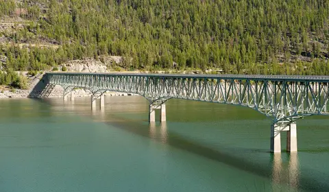 A long truss bridge crosses a reservoir surrounded by forested hills.