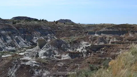 A landscape showing badlands with eroded rock formations under a clear blue sky.
