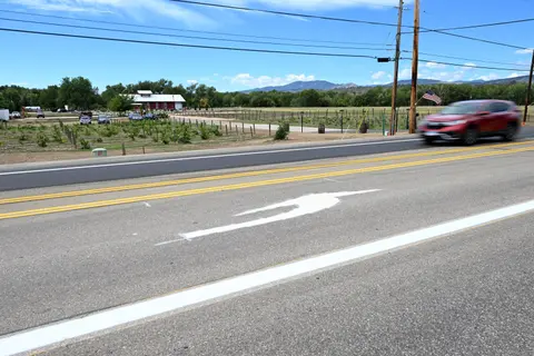 A red car drives down a paved road past a rural landscape.