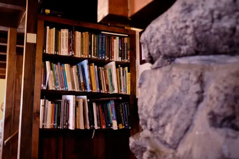 A wooden bookshelf filled with books next to a stone structure indoors.