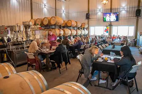 People gathered inside a winery tasting room with wine barrels and equipment.