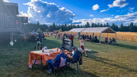 A gathering of people outside on a grassy area with tents and tables under a cloudy sky.
