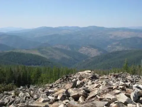 A view of forested mountains from a rocky summit.