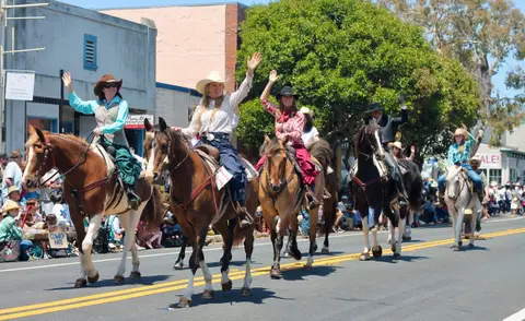 People ride horses and wave in a street parade.