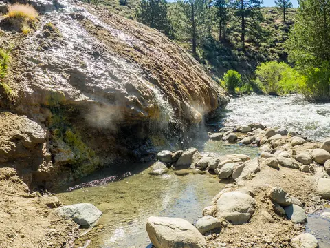 A natural hot spring pool next to a river with mineral deposits.