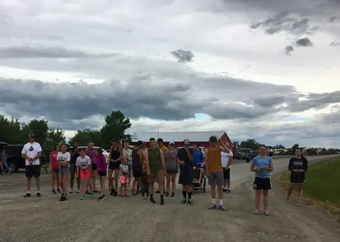 A group of people standing outside on a gravel road under a cloudy sky.