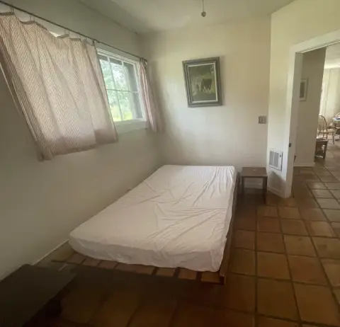A simple bedroom with a low bed, a window with curtains, and a tiled floor.