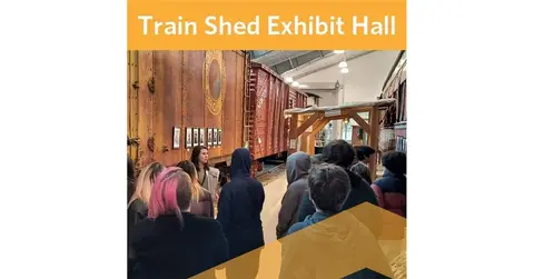 A tour group looks at a vintage train car in an exhibit hall.