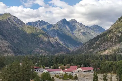 A cluster of buildings with red roofs sits in a valley beneath massive mountain peaks.