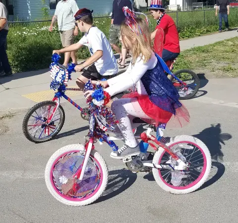 Children riding bicycles decorated with patriotic red, white, and blue decorations.