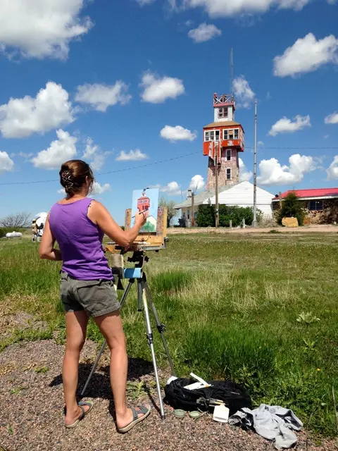 A woman paints a picture of a tall tower outdoors on an easel.