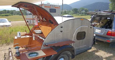 A teardrop camper trailer with its rear hatch open, revealing a built-in kitchen.