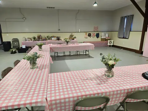 Interior view of a room with tables covered in pink and white checkered tablecloths and flower centerpieces.