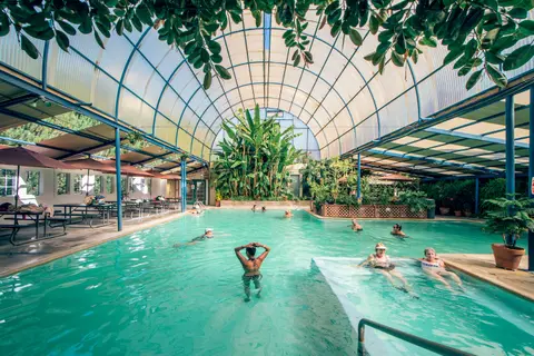 People swimming in an indoor pool under a large arched roof.