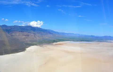 Aerial view of a vast desert landscape with mountains in the background under a blue sky.
