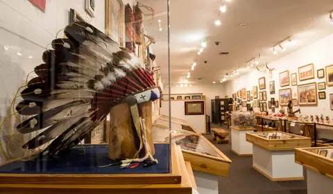 An indoor view of a museum gallery displaying artifacts including a feathered headdress in a case.