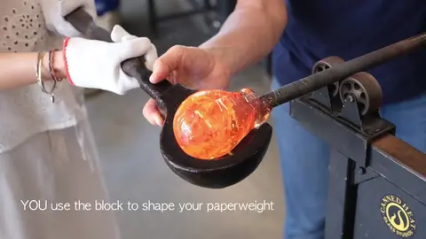 A person shapes hot glass with a block.