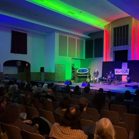 An audience seated in an auditorium watches performers on stage.