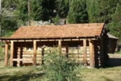 A rustic log building with a covered porch stands surrounded by trees.