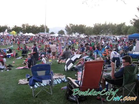 A large crowd gathers on a grassy park for an outdoor event.