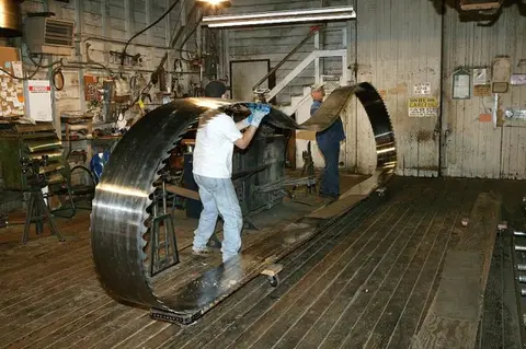 A large band saw blade being handled in an interior workshop.