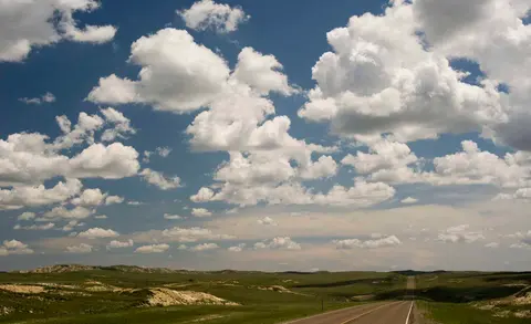 A long straight road stretching across a vast grassy plain under a partly cloudy sky.