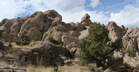 A landscape featuring weathered rock formations and green bushes under a cloudy sky.