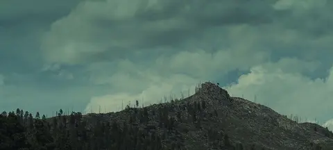 A rugged, forested mountain peak under a cloudy sky.