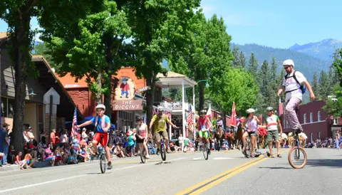 A group of unicyclists ride down a street lined with crowds during a parade.