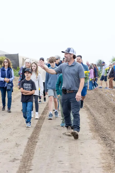 A guide leads a group of people walking outdoors on a dirt path.