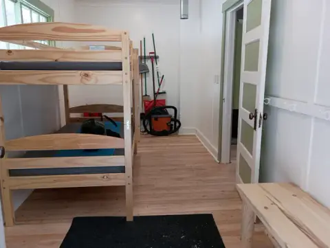 An interior shot of a room with a bunk bed, wooden floor, and cleaning supplies in the corner.
