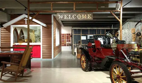 An indoor museum exhibit displays a vintage car and historical replicas.
