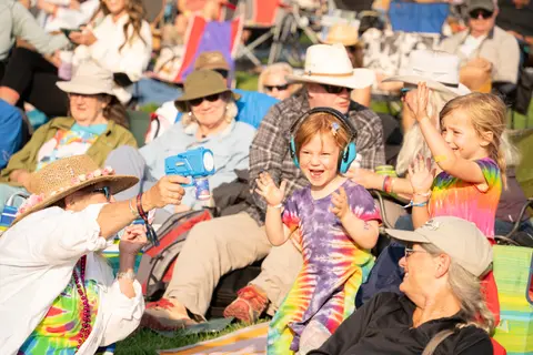 A crowd of people enjoying an outdoor event, with children playing in the foreground.