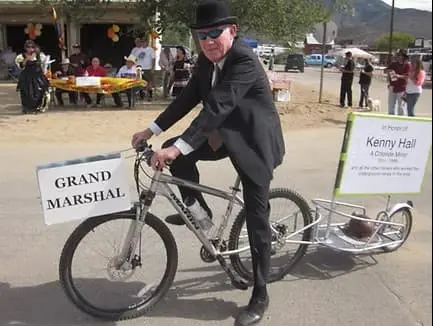 A man in a suit and bowler hat rides a bicycle with signs attached.