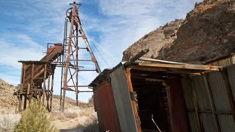 An old mining structure and a dilapidated building in a desert landscape.