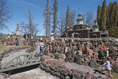 Visitors walk around an outdoor rock castle and sculpture garden.