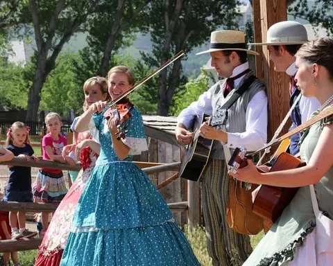 People in period costume play music outdoors while onlookers watch.