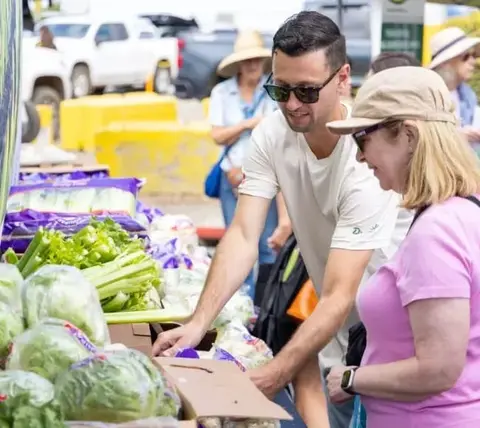 People select fresh produce at a market stand.