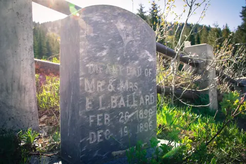 A weathered gravestone stands outdoors in a grassy area.