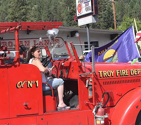 A woman sits in the driver's seat of a vintage red fire truck during an event.