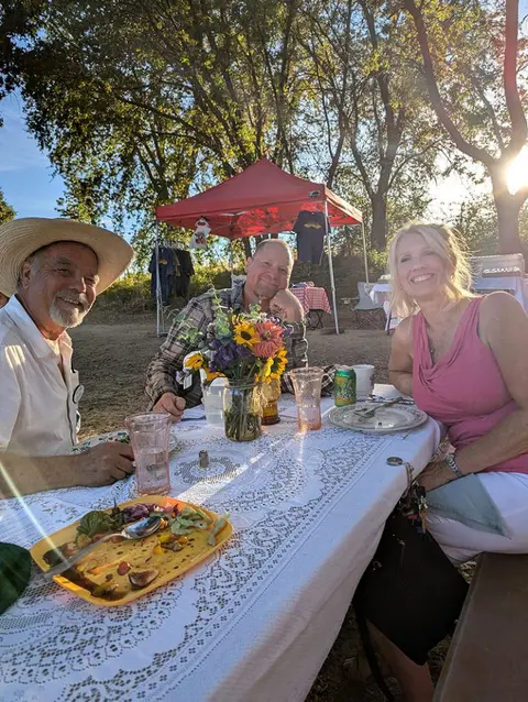 Three people sit together at an outdoor dining table.